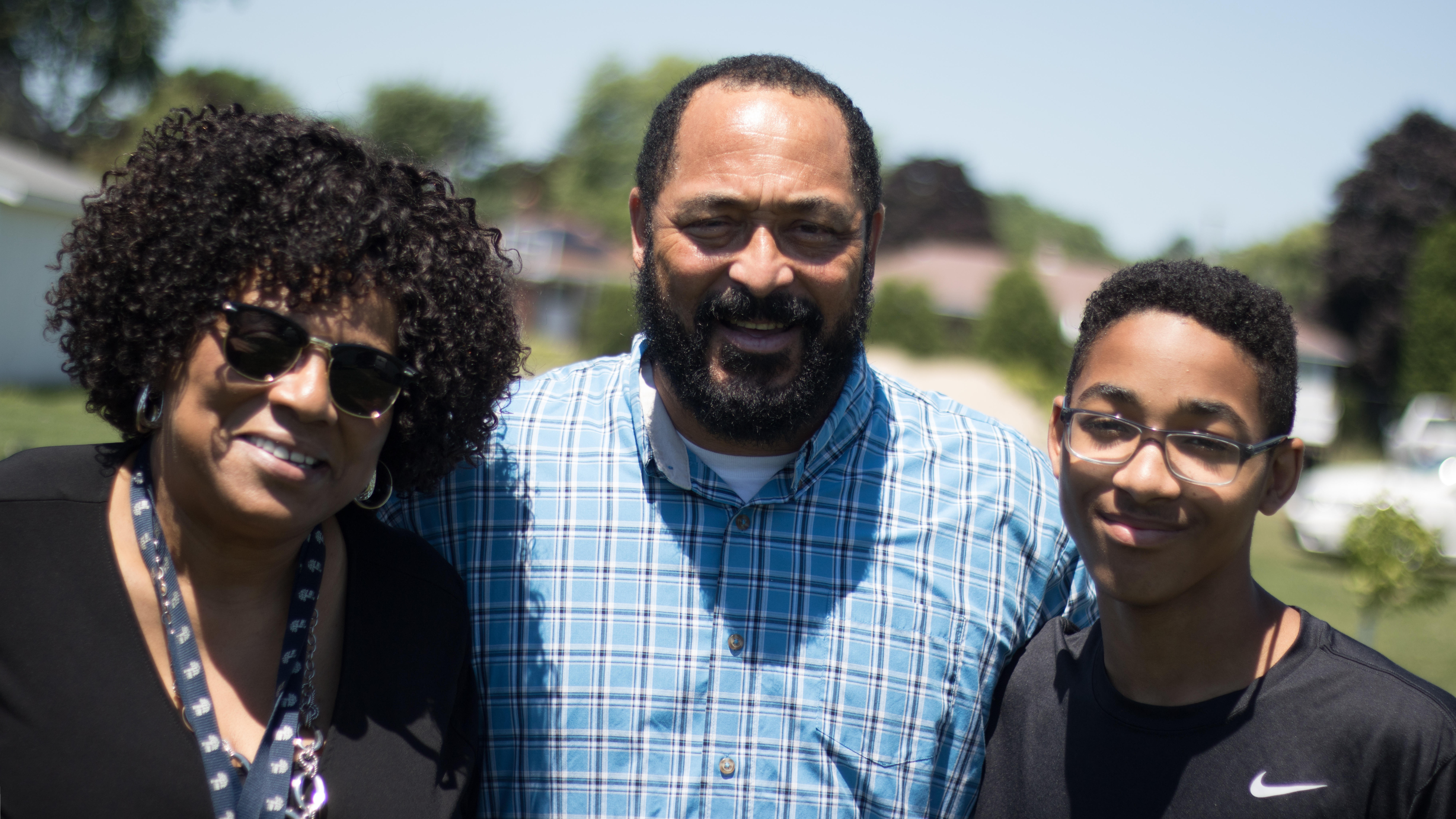 Community engagement coordinator posing for a photo with a father and son at an outdoor event.